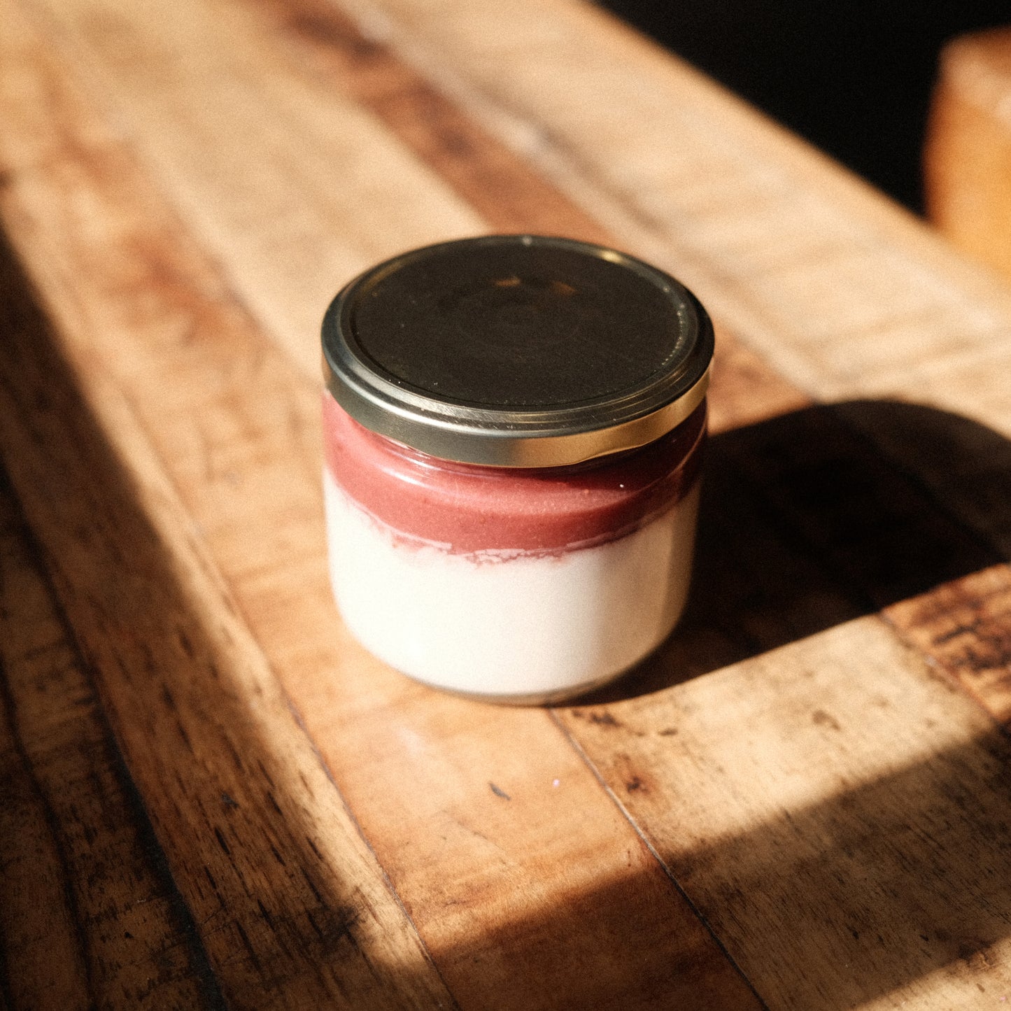 12oz glass jar with gold lid. Two-thirds filled with coconut panna cotta custard and one third top is strawberry compote puree.