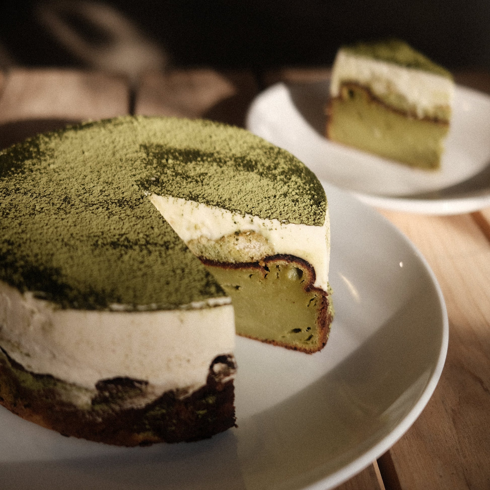 Whole matcha tiramisu basque cheesecake with a slice cut out of it on white plates