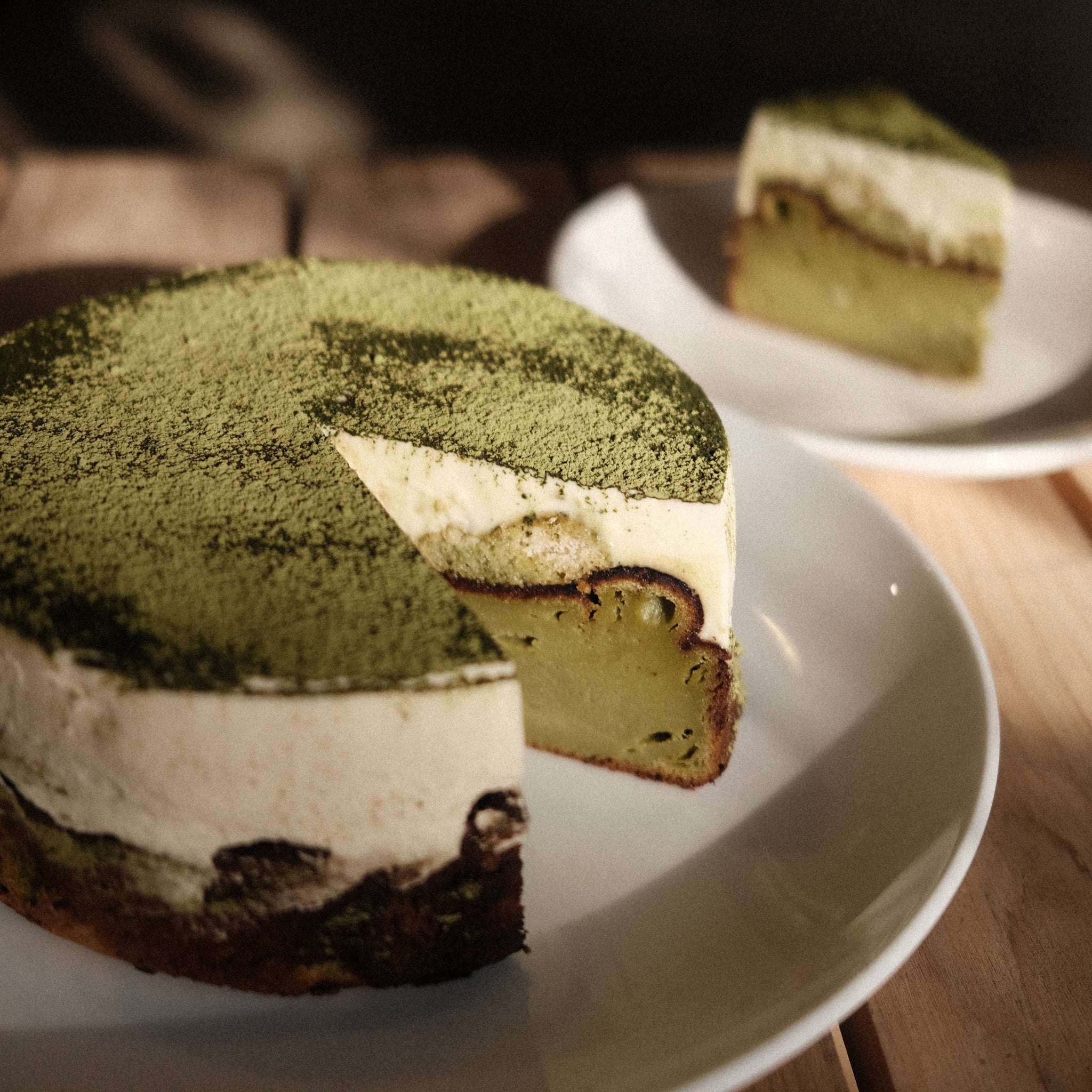 Whole matcha tiramisu basque cheesecake with a slice cut out of it on white plates