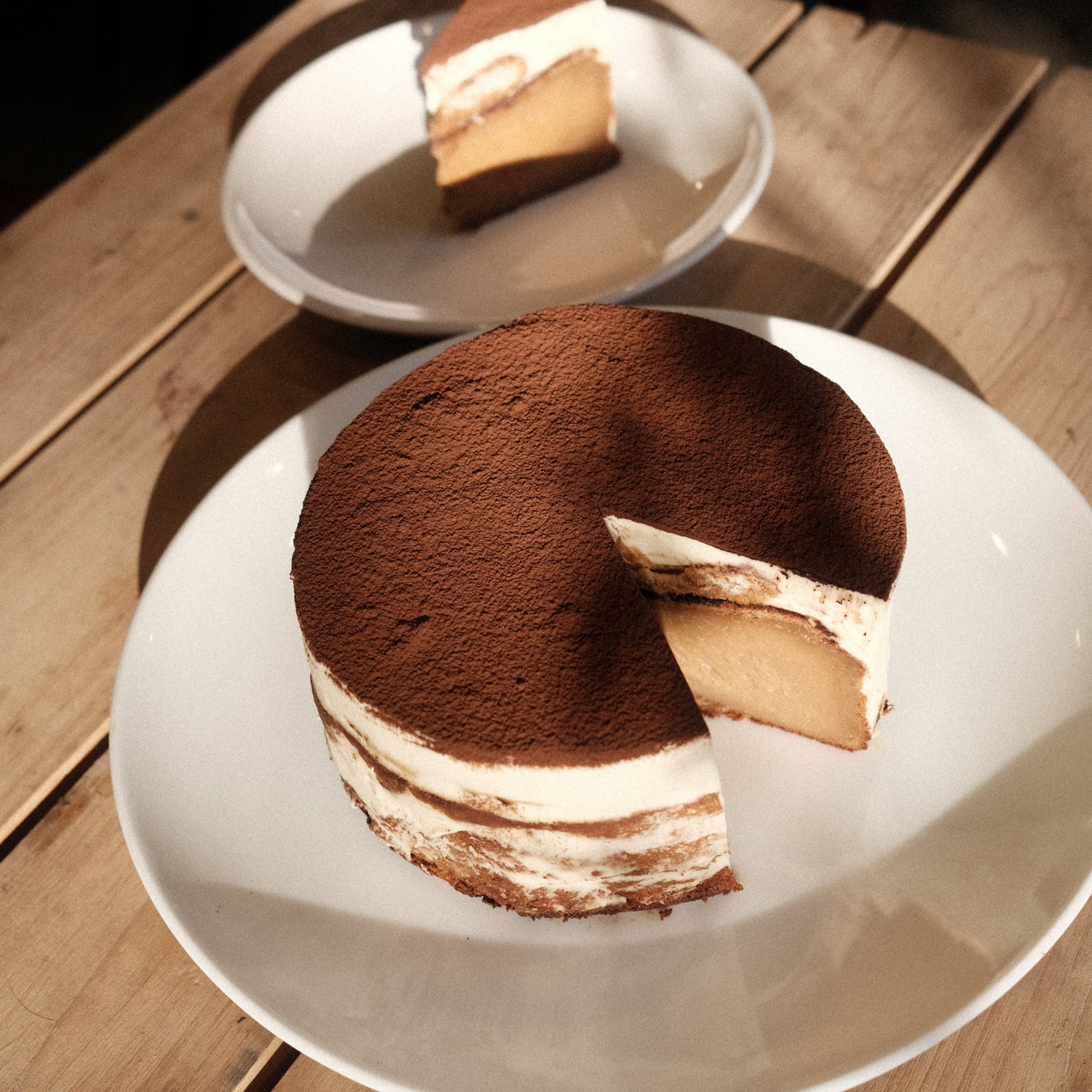 A whole Vietnamese coffee tiramisu basque cheesecake with a slice cut out on white plates