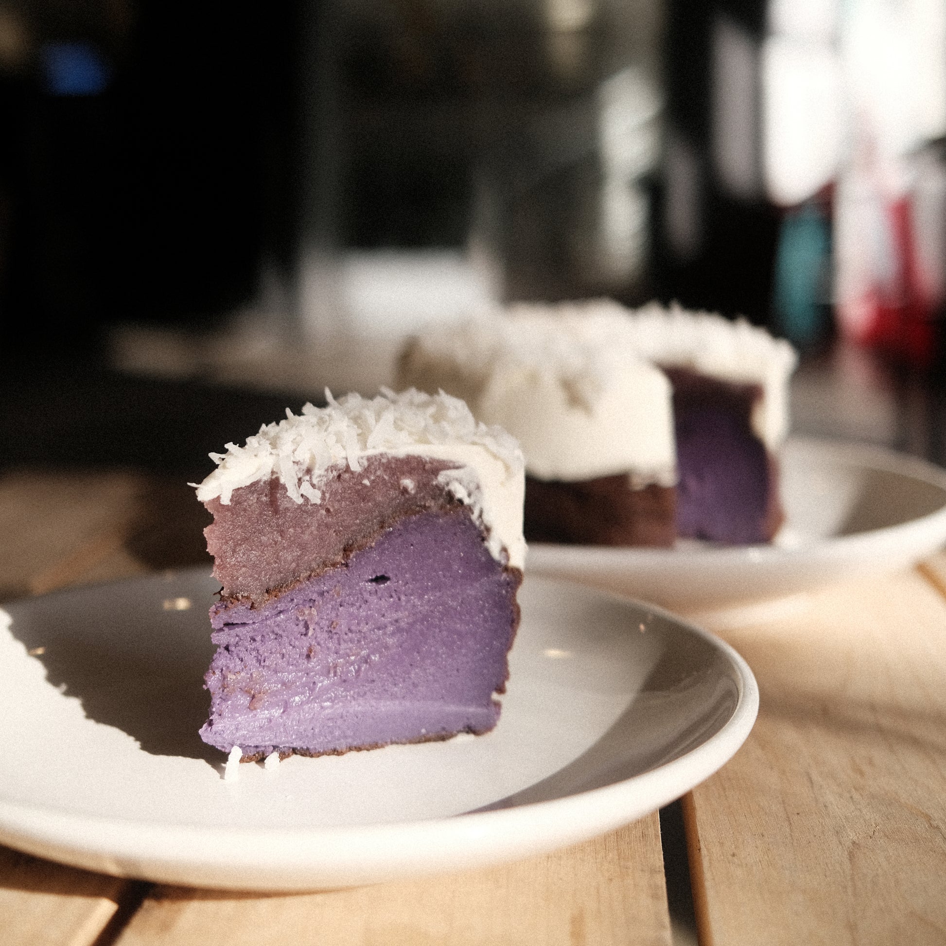 A slice of ube basque cheesecake and the rest of the cake in the background on white plates